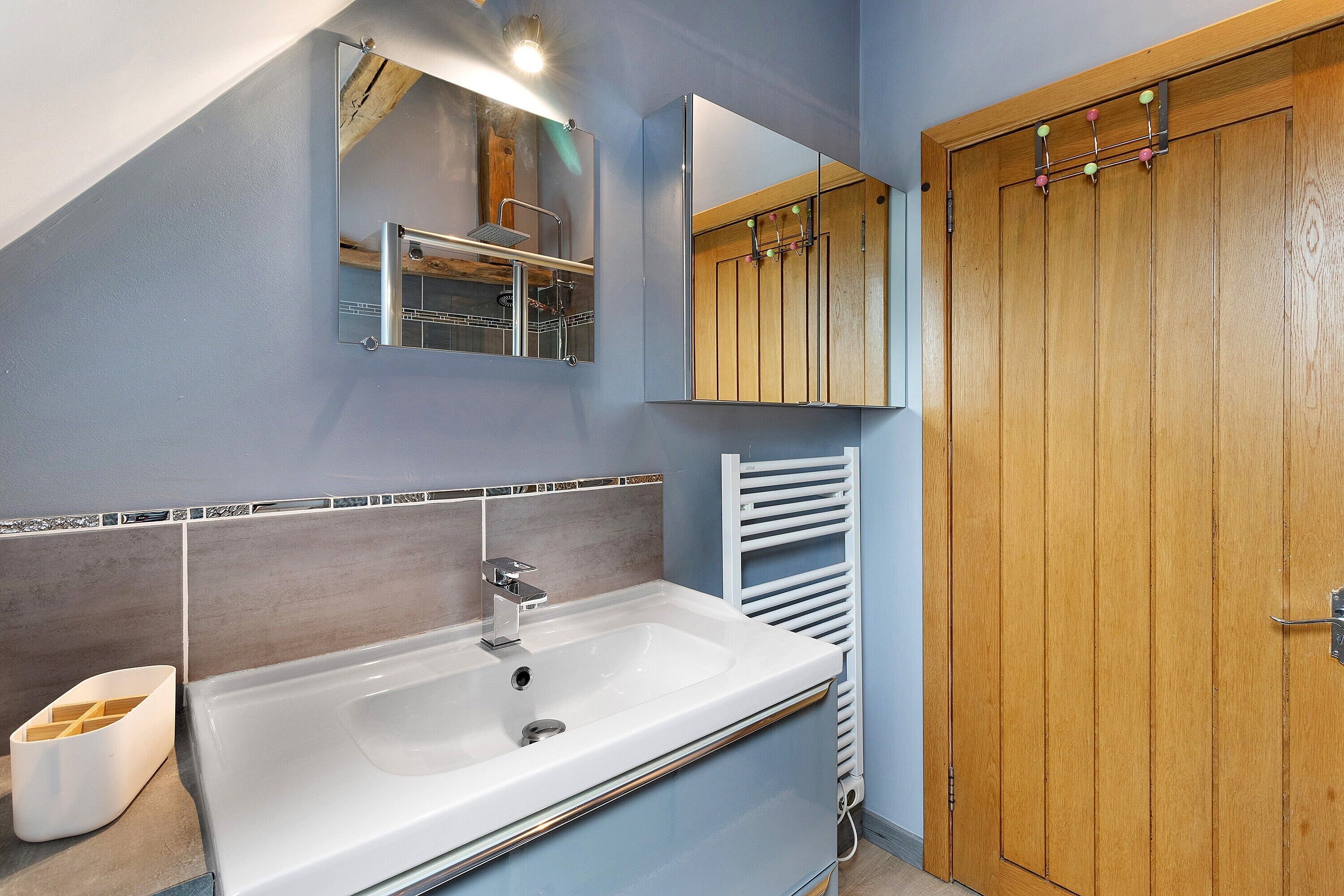 Een badkamer met een wit wastafel, een spiegel en een houten deur.