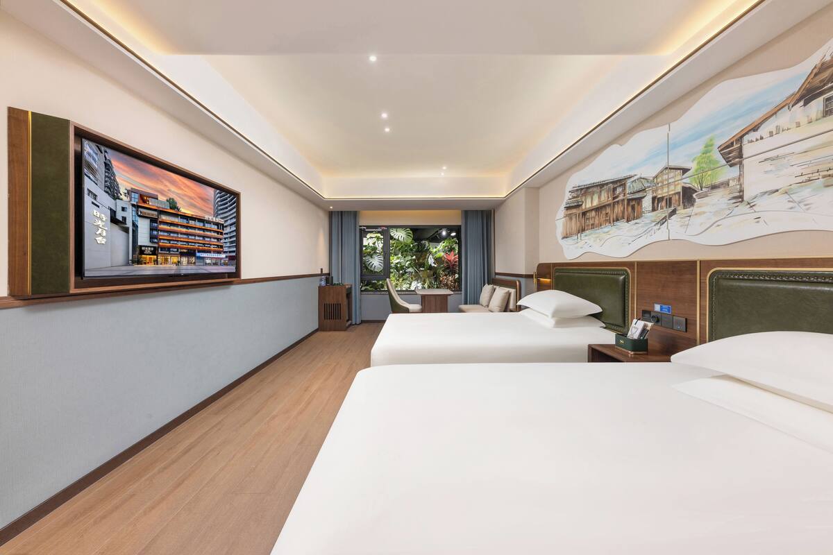 Habitación de hotel con dos camas, un escritorio, una silla, un televisor y un cuadro en la pared.