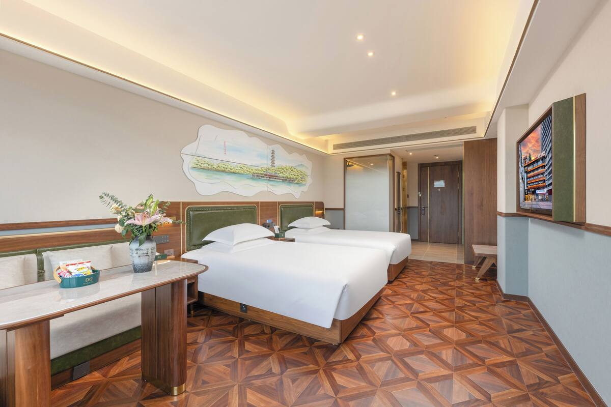 Una habitación de hotel con una cama, un escritorio, un florero con flores y un cuadro en la pared.
