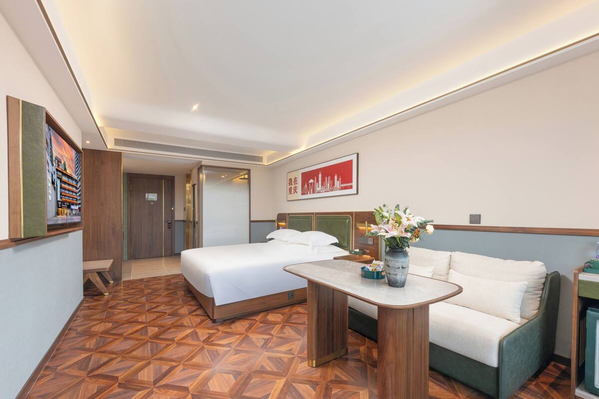 Habitación de hotel con dos camas, un sofá, una mesita con un florero y un cuadro en la pared.