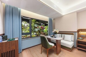 A hotel room with a window view of greenery, a sofa, a small table, and a wooden desk. - Nostalgia Hotel chongqing hongyadong (Chongqing)