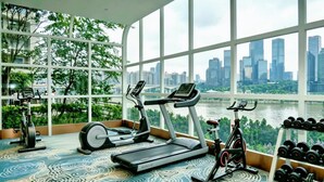 Ein Fitnessstudio mit Laufbändern, Crosstrainern und Fahrrädern, mit einem großen Fenster mit Blick auf eine Stadtlandschaft.