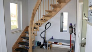 Eine Holztreppe führt zu einer Zwischenebene mit einer Bank und einem Staubsauger.