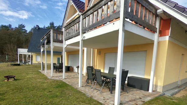 Ein zweistöckiges Gebäude mit einer überdachten Terrasse, Außenbestuhlung und einer Garage.