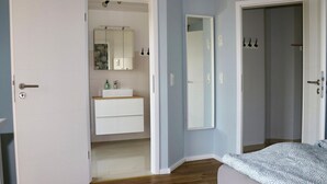 Ein Schlafzimmer mit Bett, Nachttisch, Spiegel und einer Tür zu einem Badezimmer.