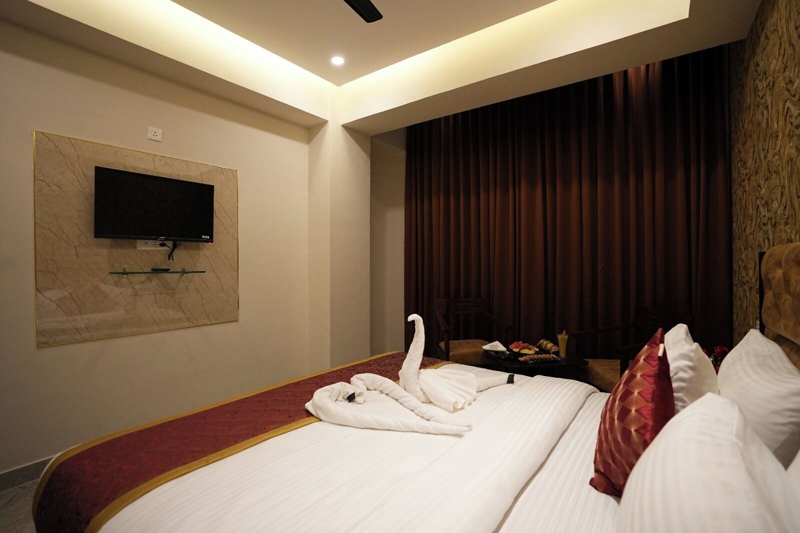 A hotel room with a large bed, a flat-screen TV mounted on the wall, and a wooden headboard.