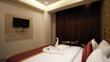 A hotel room with a large bed, a flat-screen TV mounted on the wall, and a wooden headboard.