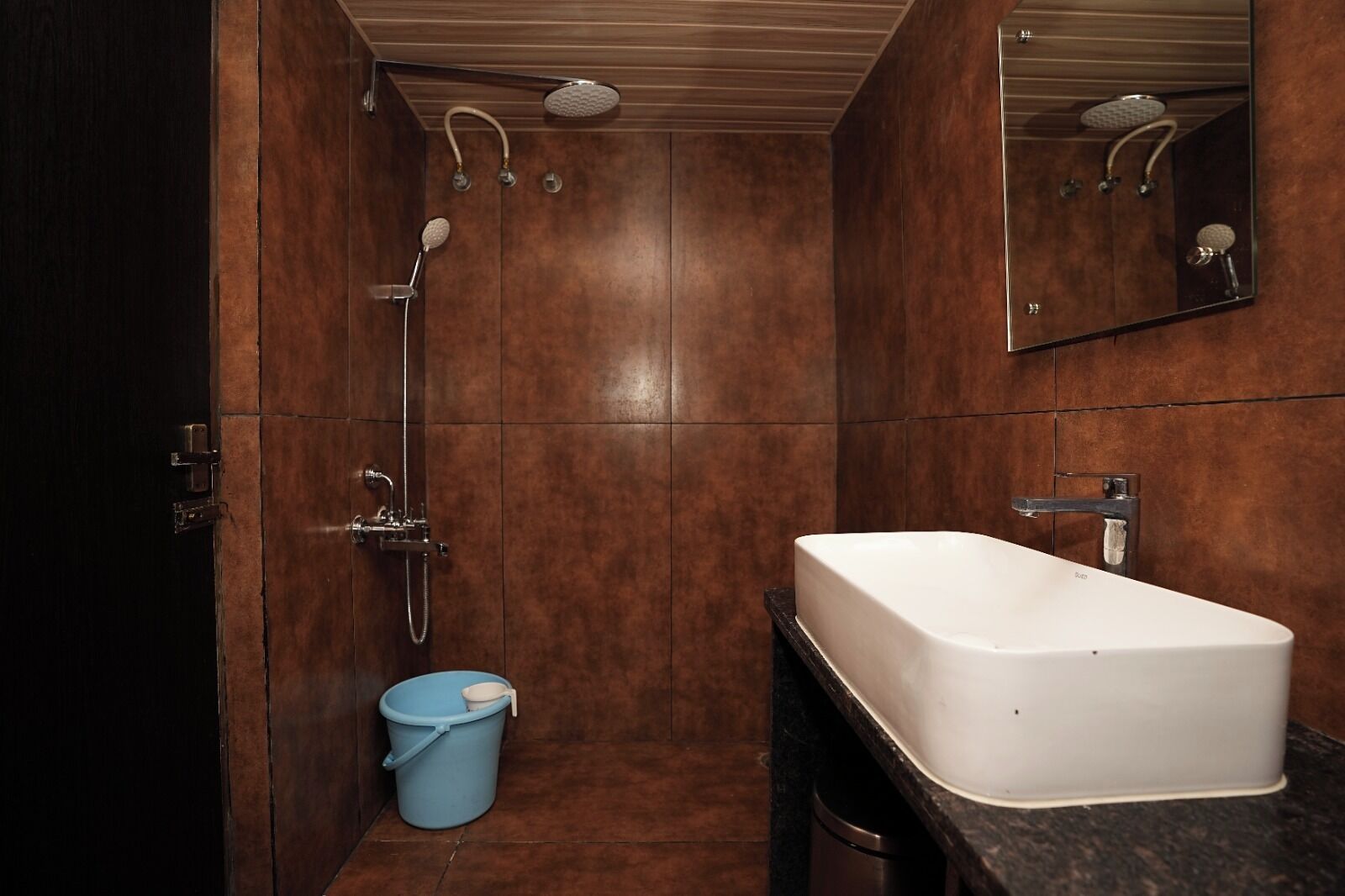 A bathroom with a white sink, a shower with a handheld showerhead, and a blue bucket.