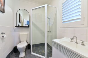 A modern bathroom with a toilet, a glass-enclosed shower, and a sink with a mirror above it. - Lamp Estate (Lovedale)