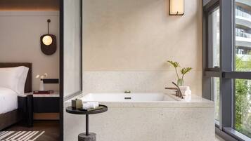 A modern bathroom with a large bathtub, a small round table, and a nightstand with a book and a vase of flowers.