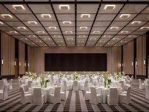 A large conference room with a high ceiling, multiple tables set for events, and a large screen at the front.