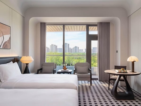 A hotel room with a bed, two chairs, a small table, and a view of the cityscape through large windows. - Kimpton Nine Trees Shanghai by IHG (Shanghai)