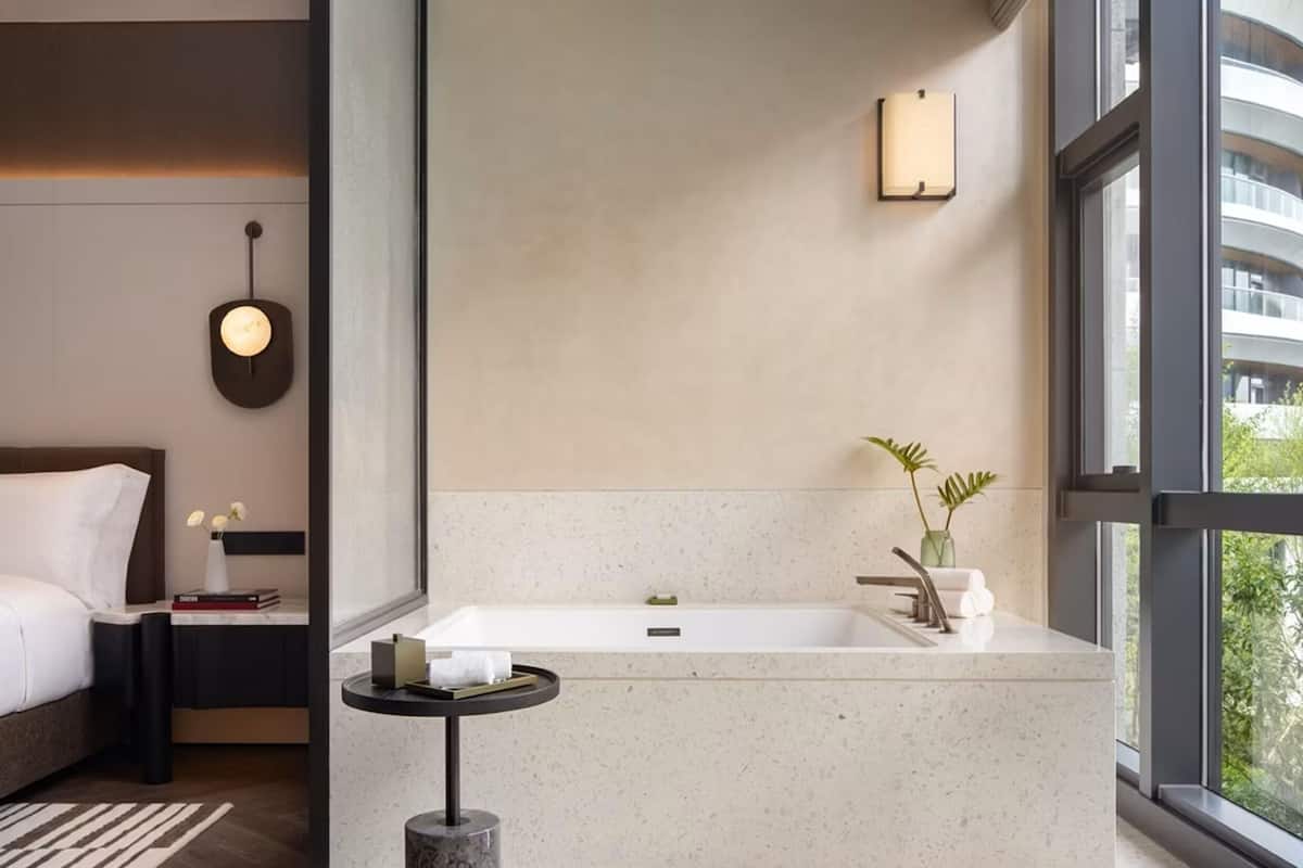 A modern bathroom with a large bathtub, a small round table, and a nightstand with a book and a vase of flowers.