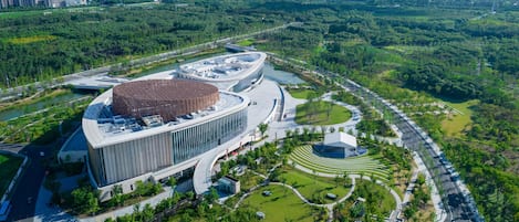 A modern building with a circular central structure, surrounded by landscaped gardens and a river.