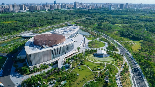 A modern building with a circular central structure, surrounded by landscaped gardens and a river.