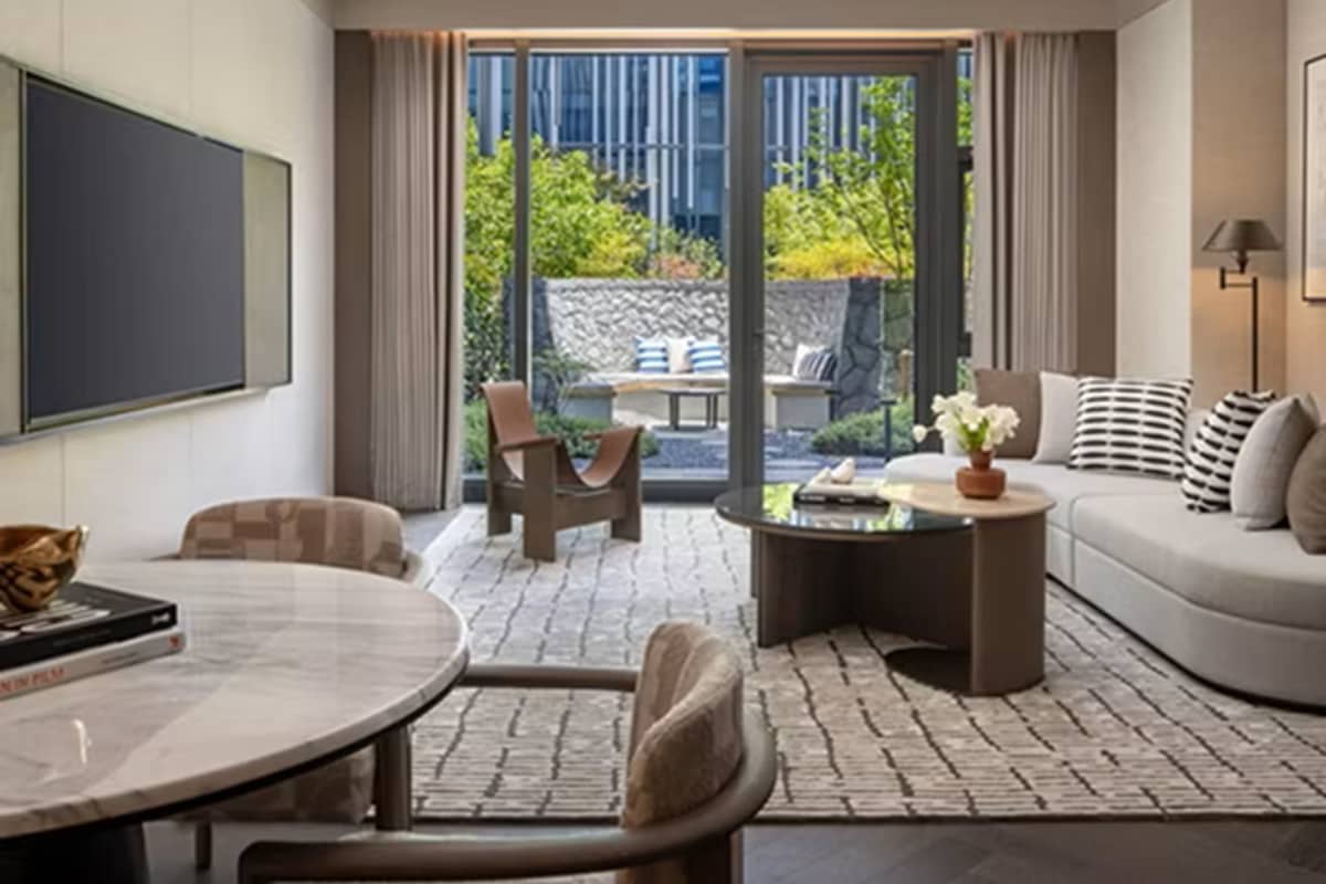A modern living room with a sofa, coffee table, and chairs, a flat-screen TV, and a view of greenery outside.