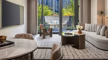 A modern living room with a sofa, coffee table, and chairs, a flat-screen TV, and a view of greenery outside.