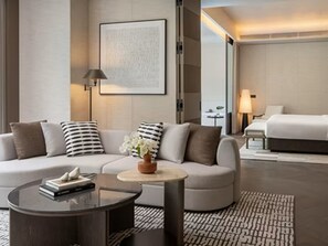 A modern hotel room with a sofa, a round coffee table, a bed, and a framed artwork on the wall.