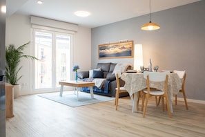 A modern living room with a sofa, dining table, chairs, a lamp, and a large window.