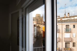 A view through a window of a narrow street with buildings, including a church with a bell tower, and balconies with railings.