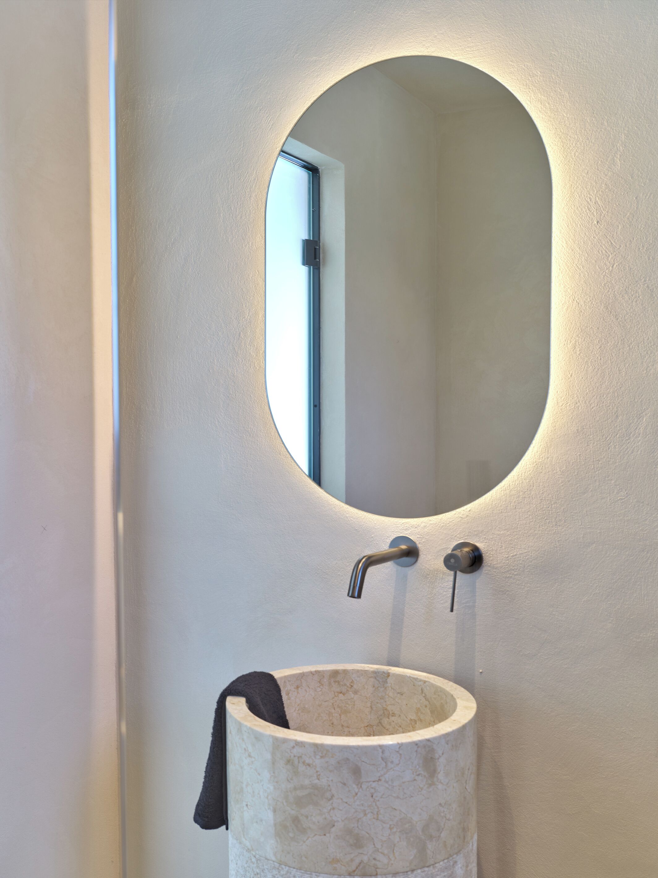 Un bagno con uno specchio rotondo, un lavandino e un asciugamano appeso al muro.