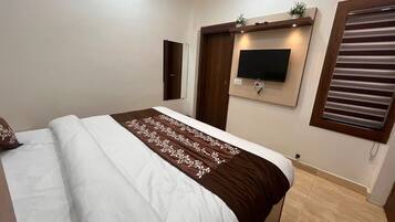 A bedroom with a bed, a television mounted on the wall, and a window with blinds.