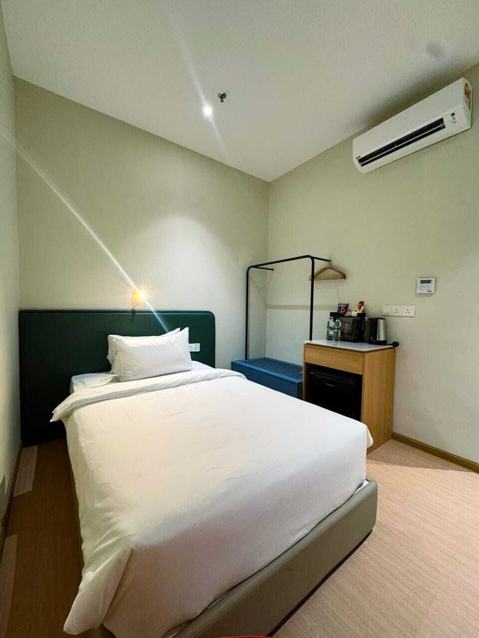 Habitación de hotel con cama, mesita de noche, lámpara, equipo de aire acondicionado y un pequeño escritorio con silla.
