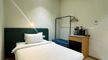 Habitación de hotel con cama, mesita de noche, lámpara, equipo de aire acondicionado y un pequeño escritorio con silla.