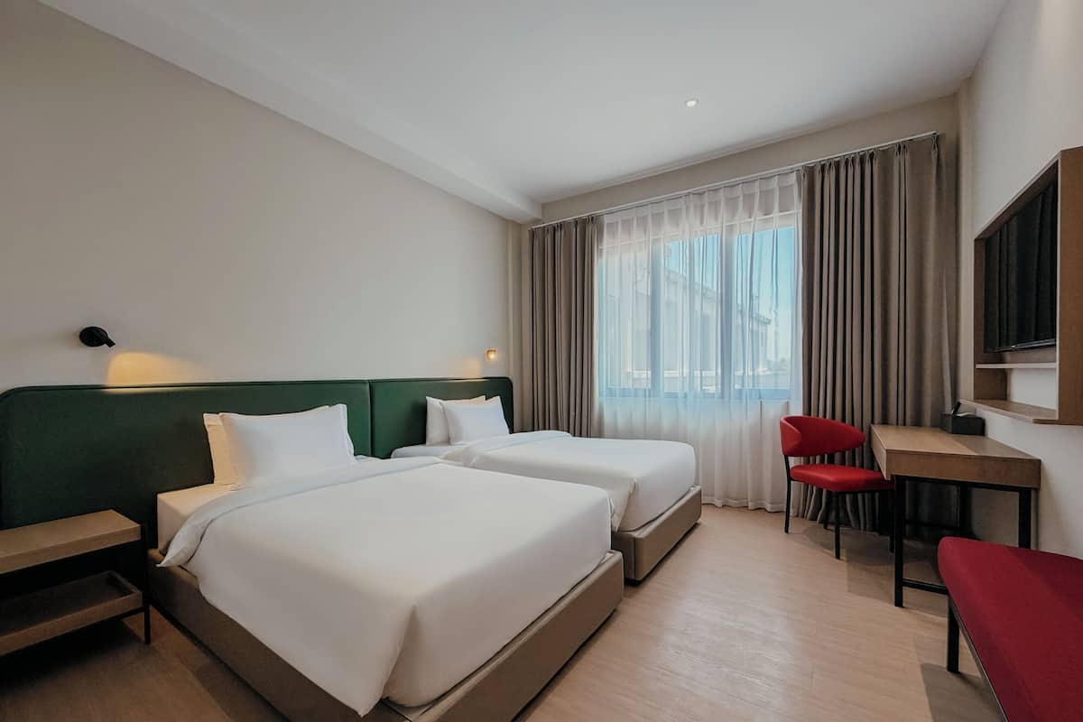 A hotel room with two beds, a desk, a chair, and a TV.