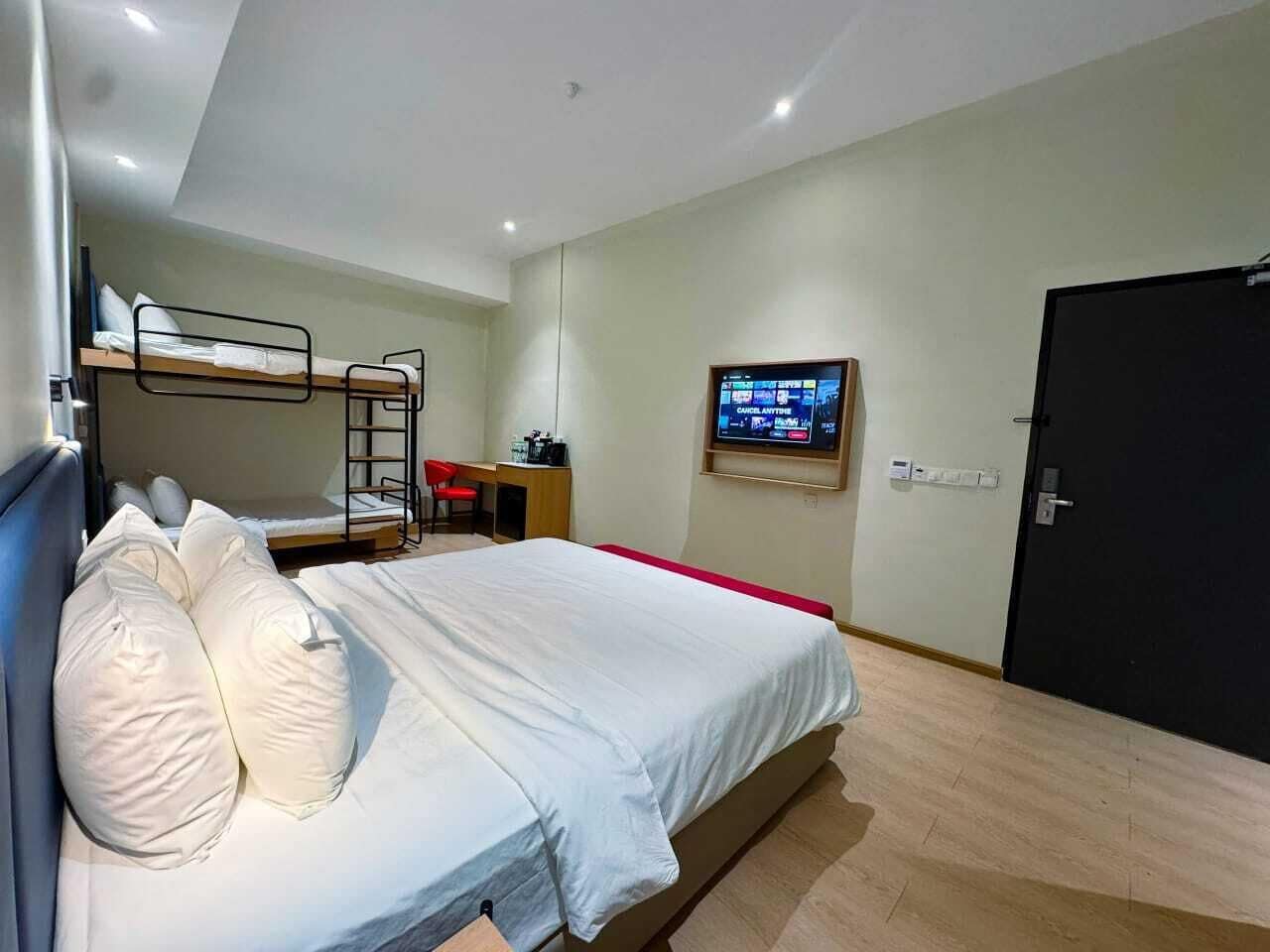 A bedroom with a bunk bed, a desk with a chair, a television mounted on the wall, and a door.