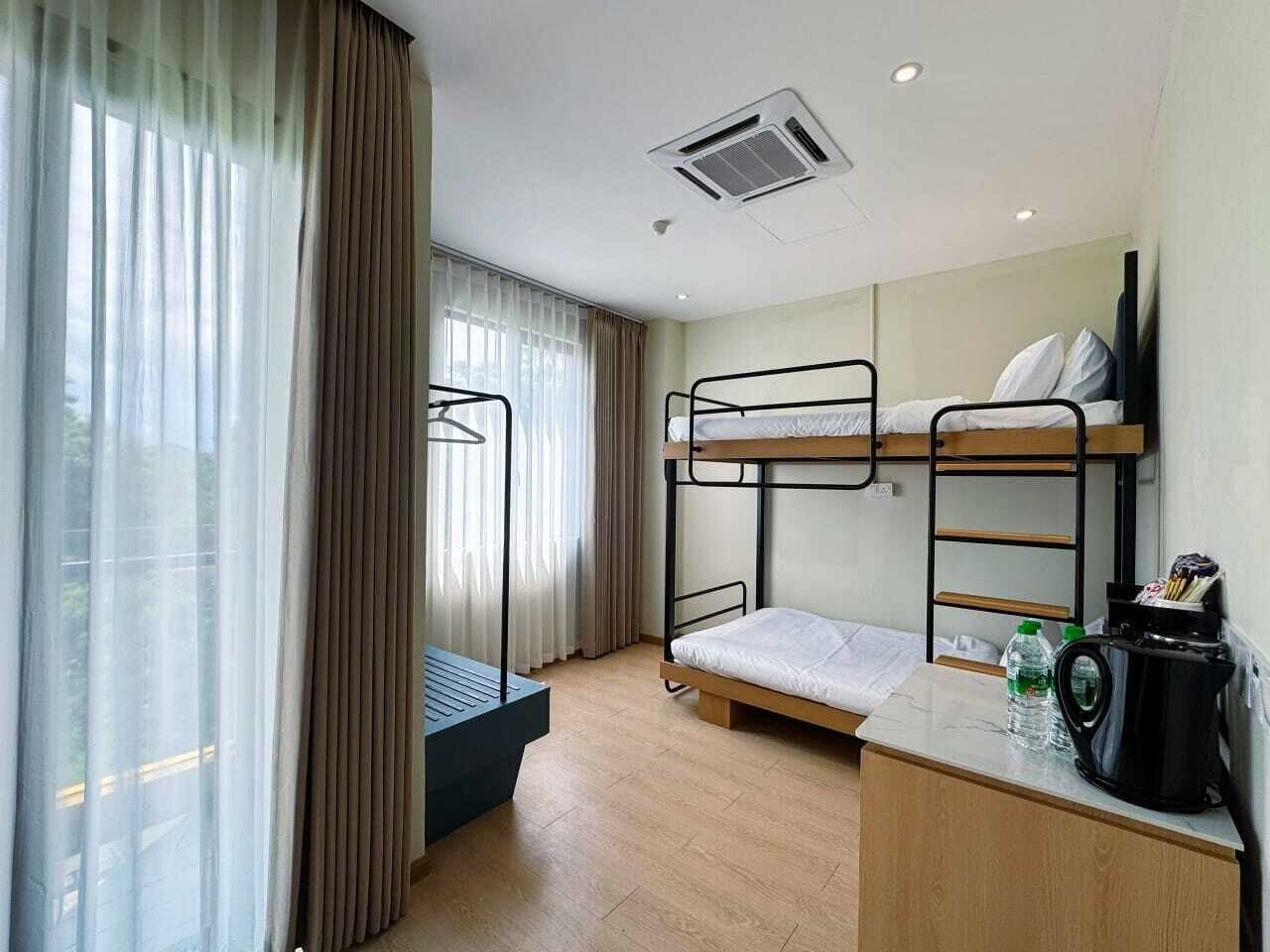 A compact hotel room with bunk beds, a desk, a chair, and a window with curtains.