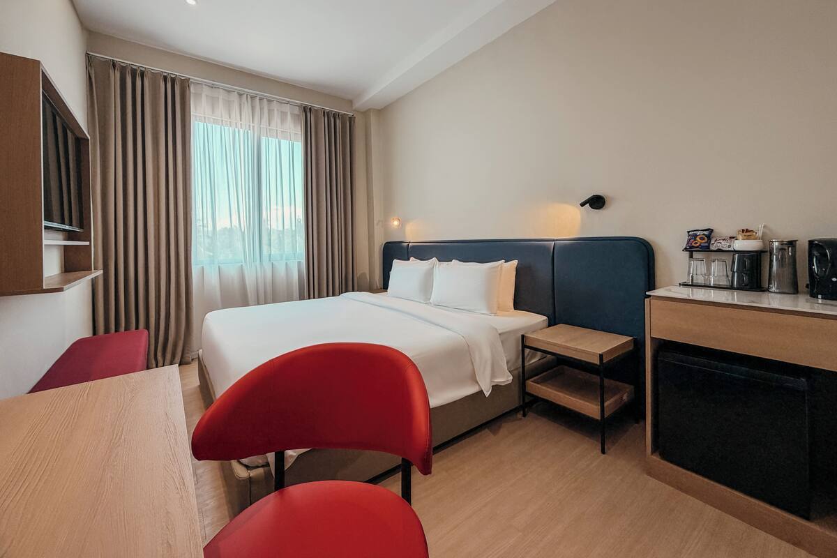 A hotel room with a bed, a desk with a coffee maker, a chair, and a TV.