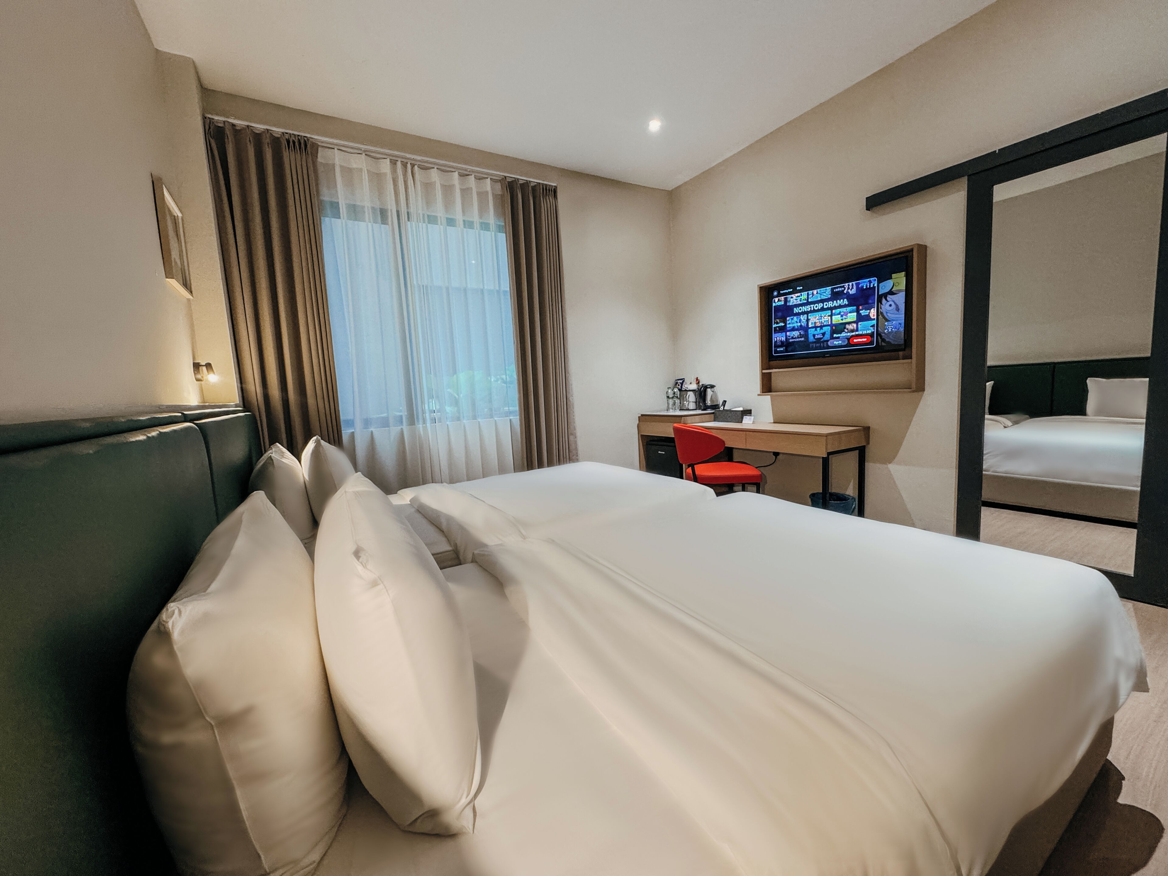 A hotel room with a bed, a desk, a chair, a television, and a window with curtains.