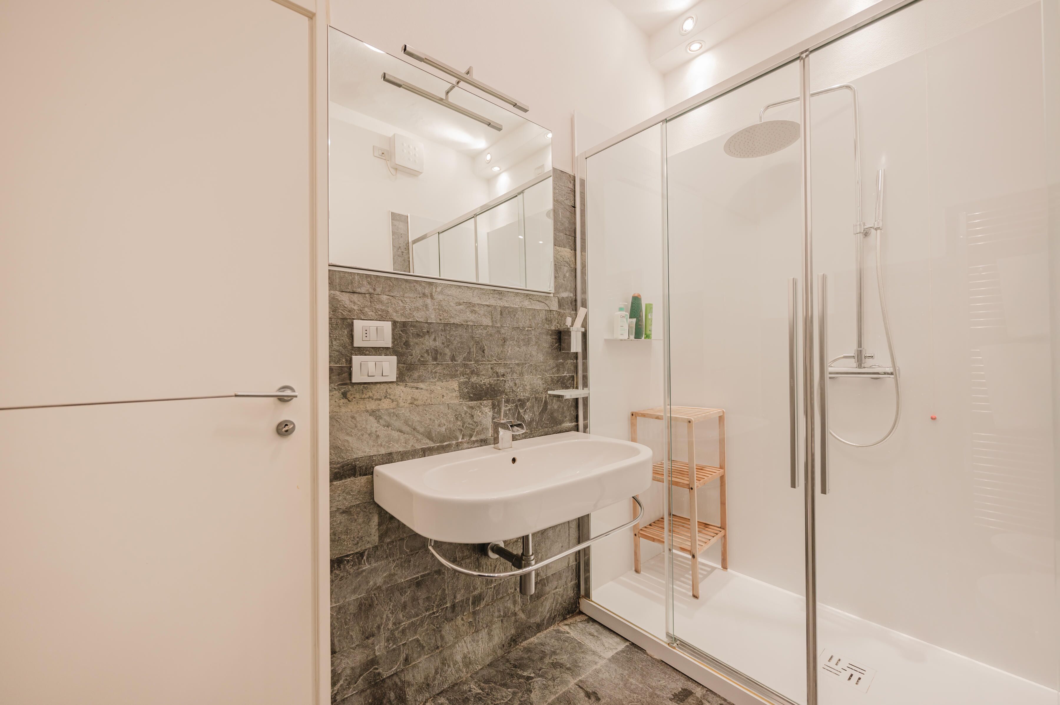 Ein modernes Badezimmer mit Duschkabine aus Glas, einem weißen Waschbecken und einer Marmor-Spritzschutzwand.