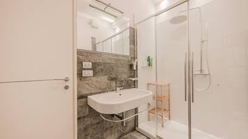 Ein modernes Badezimmer mit Duschkabine aus Glas, einem weißen Waschbecken und einer Marmor-Spritzschutzwand.