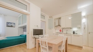 Ένα μικρό δωμάτιο με ένα κρεβάτι, μια τηλεόραση, ένα τραπέζι φαγητού με καρέκλες, μια μικρή κουζίνα και ένα μεγάλο παράθυρο.