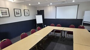Una sala conferenze con un lungo tavolo, sedie rosse, una lavagna e uno schermo per proiettore.