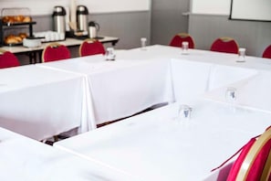 A conference room with white tables, red chairs, and a projector screen in the background.