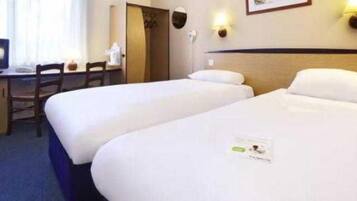 A hotel room with two single beds, a desk with a chair, a television, and a small table.
