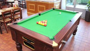 A pool table with balls, wooden chairs, and a bar area.