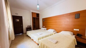 Habitación de hotel con dos camas, cabecero de madera, mesita de noche con teléfono, armario y lámpara en el techo.