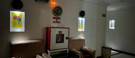 A waiting area with two armchairs, a small table, a fire alarm, and a wall-mounted clock.
