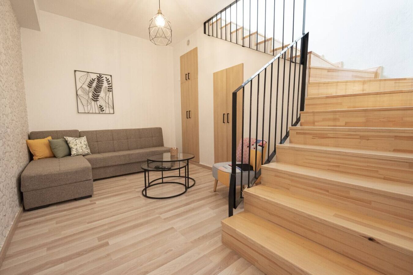 A modern living room with a sofa, a glass coffee table, and a staircase with wooden steps.