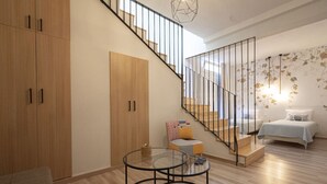 Un interior moderno con una escalera, suelo de madera, una mesa de cristal y una cama con diseño floral en la pared.