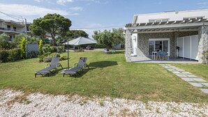 Ein modernes Haus mit Naturstein-Fassade, einer überdachten Terrasse mit Gartenmöbeln und einem gepflegten Rasen.