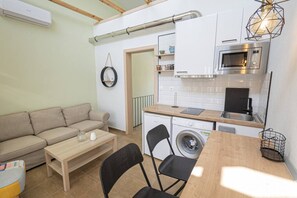 Un espacio habitable compacto con sofá, mesa de madera, lavadora, microondas y lavamanos.