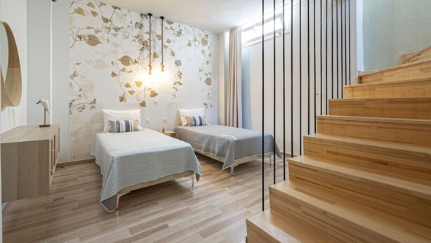 Ein Schlafzimmer mit zwei Betten, einer Holztreppe und einer Wand mit Blattmustern.