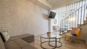 Ein modernes Wohnzimmer mit Steinwand, einer Couch, einem Glastisch, einem Sessel und einer Treppe mit Geländer.
