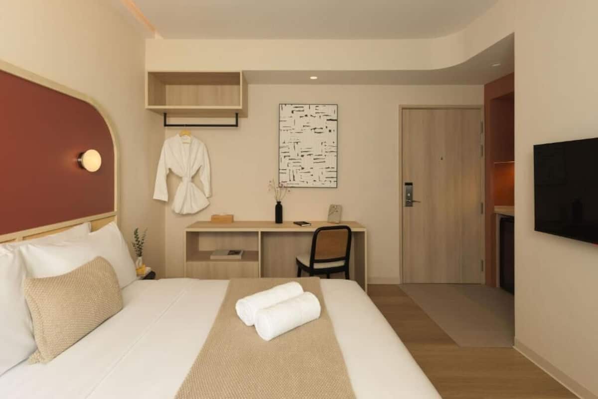 Una habitación de hotel con cama, escritorio, silla, televisor y puerta.