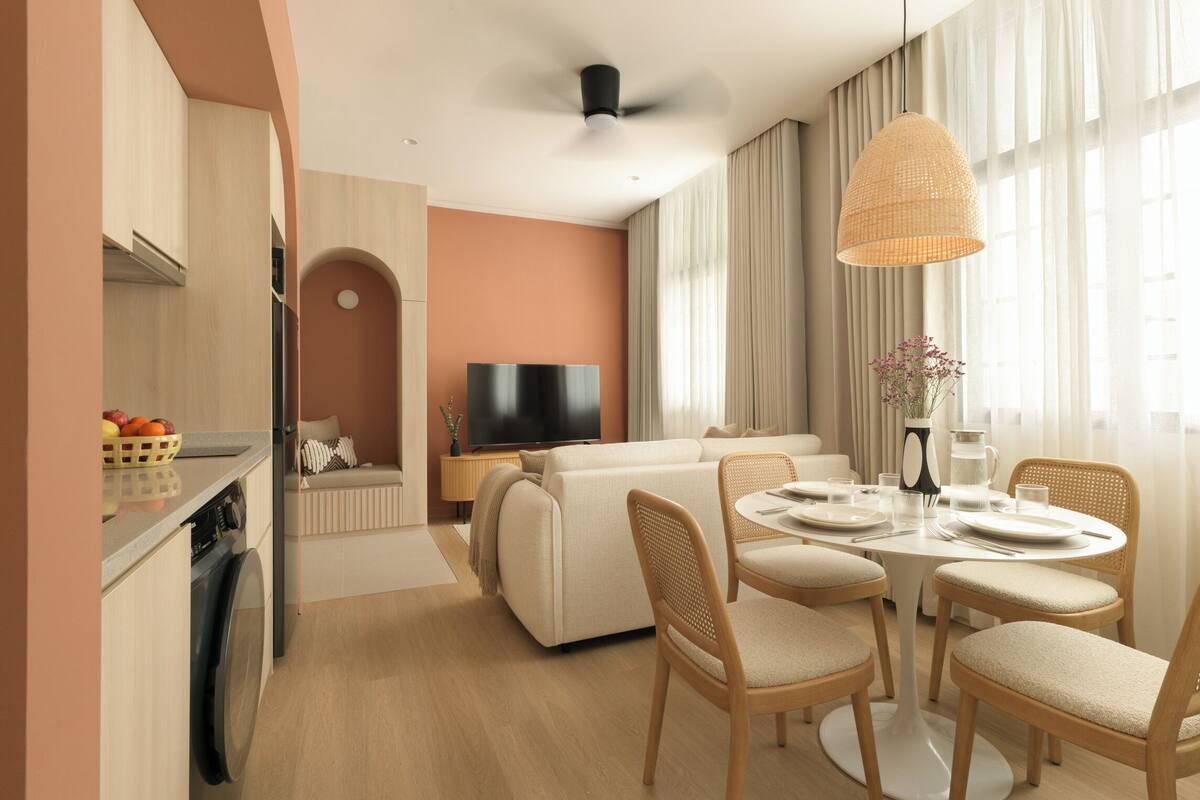 Una sala de estar moderna con sofá, mesa de comedor, sillas, televisor y zona de cocina con lavadora.